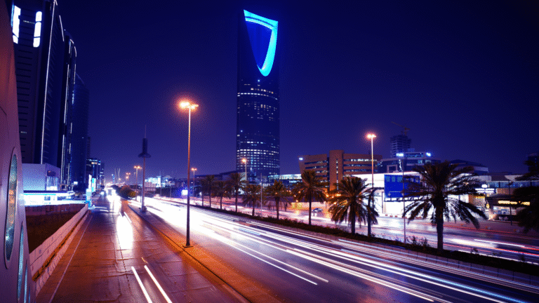 The Kingdom Centre Tower at night in Riyadh, seen from the highway with palm trees and car light trails, illustrating the urban life for Expatriates in Riyadh.