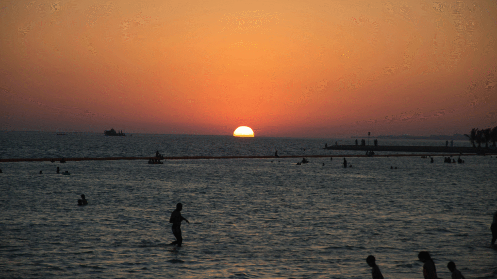 Sunset at Yanbu Al Bahr beach with silhouettes of people swimming in the Red Sea.