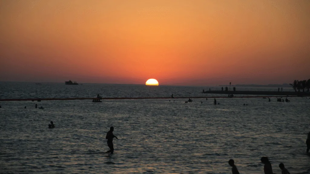 Sunset at Yanbu Al Bahr beach with silhouettes of people swimming in the Red Sea