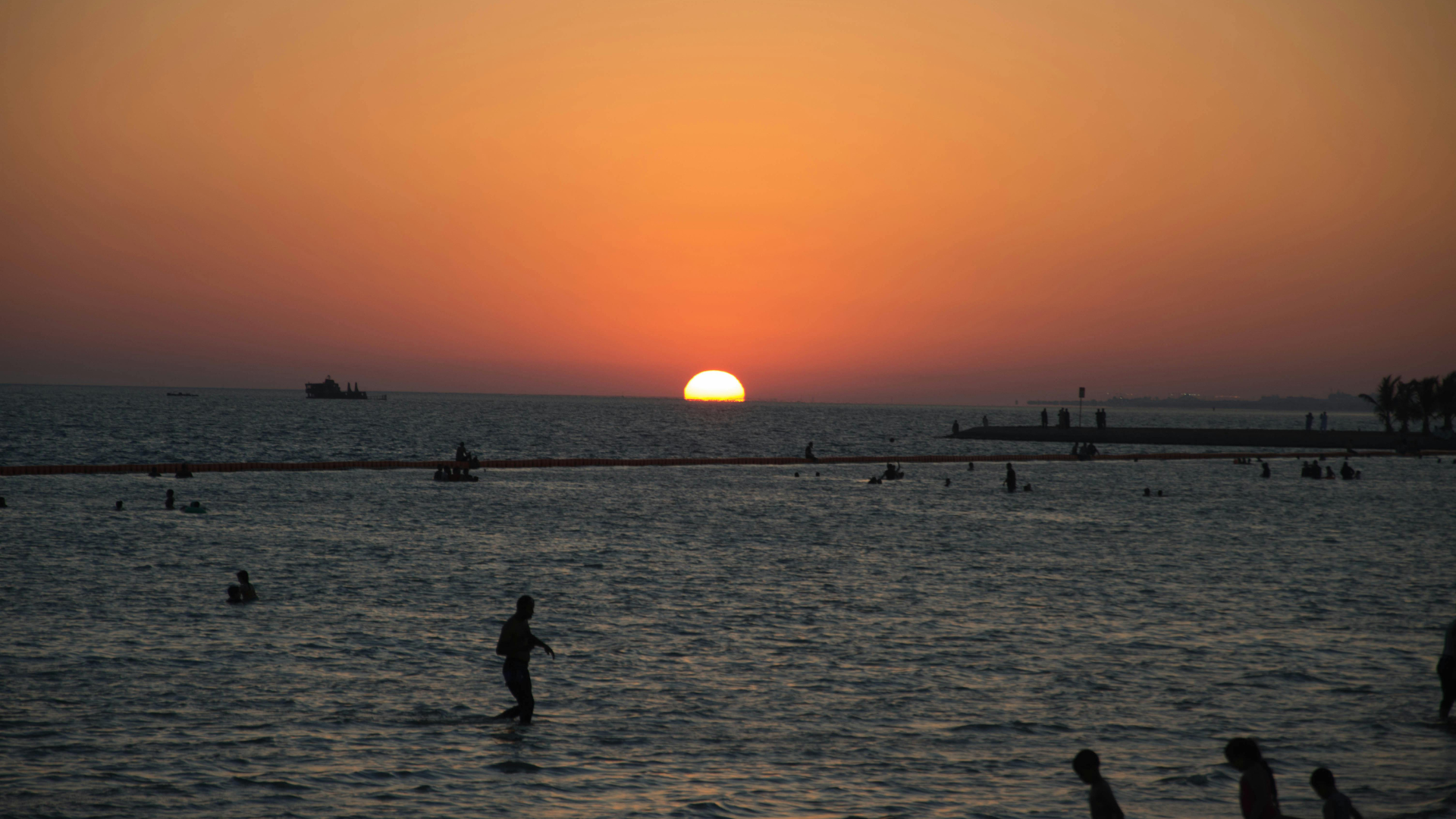 Sunset at Yanbu Al Bahr beach with silhouettes of people swimming in the Red Sea